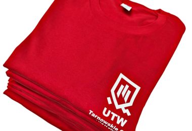 Stos czerwonych koszulek z białym logo UTW